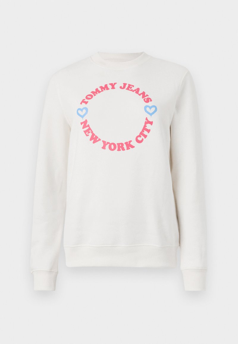 Sweatshirt blanc avec un graphique rond portant "TOMMY JEANS" en rose et "NEW YORK CITY" en dessous, agrémenté de coeurs bleus. Tissu en coton doux.
