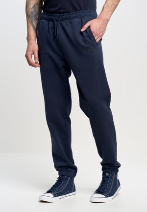 Marineblauwe joggingsbroek van zacht materiaal, met een elastische tailleband, zijzakken en taps toelopende boorden. Inclusief een subtiele logo-detail.