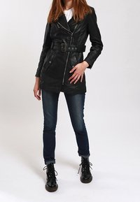 Černá kožená bunda s opaskem v pase, zipovým zapínáním, šikmými kapsami a klopovým límcem. Nositelná přes bílé triko a v kombinaci s tmavými džíny.