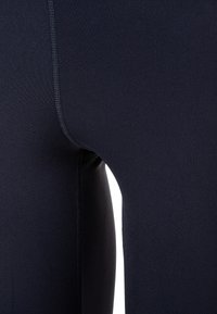Leggings marine en tissu extensible, dotés d'une texture lisse et de coutures visibles le long des joints. Vue en gros plan de l'ajustement.