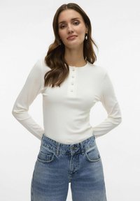 Valge pikakä sleeves top ümara kaelusega ja nööbiga, koos kõrge taljega siniste denimpükstega, millel on pleekinud viimistlus ja taskud.