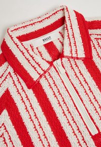 Top de punto a rayas rojas y blancas con cierre de cremallera y cuello con solapa. La tela presenta un patrón texturizado. La etiqueta dice "BALLY SUIZA."