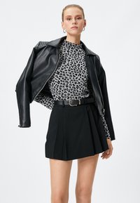 Giubbotto di pelle nera sopra una maglietta grigio leopardata, abbinato a una mini gonna plissettata nera. Presenta una fibbia metallica e orecchini a cerchio.