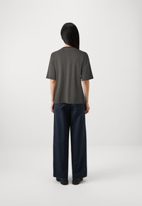 Tumši pelēkas īsām piedurknēm T-kreklā ar brīvu piegriezumu, kopā ar brīviem tumši ziliem biksēm. Audums izskatās gluds, ar minimālām dizaina detaļām.