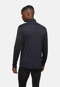 Black long-sleeve athletic shirt with a high collar, featuring contrasting textured sleeves and a fitted design. Clean, minimalist style.