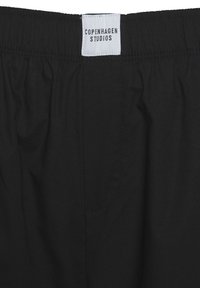 Mustat kangashousut, joissa on elastinen vyötärö ja valkoinen etiketti, jossa lukee "COPENHAGEN STUDIOS." Sujuva pinta eikä näkyviä kuvioita.