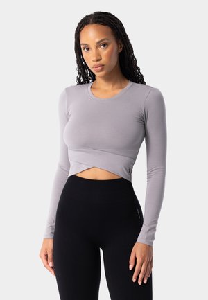 Long-sleeve gray crop top with a wrap design and smooth texture, paired with high-waisted black leggings featuring a subtle logo.