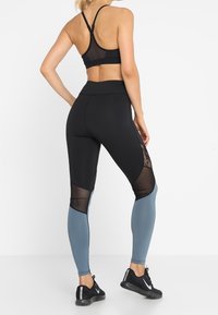 Leggings sportivi neri con pannelli in rete e accenti blu, abbinati a un reggiseno sportivo in rete nera. Presentano un design aderente e una fascia elastica in vita.