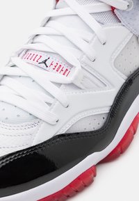 Gros plan d'une chaussure Nike Air Jordan blanche, noire et rouge avec des lacets blancs et un logo Jumpman sur l'étiquette de la languette.