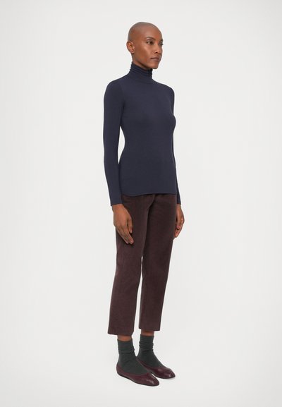 Granatowy sweter typu golf, dopasowany fason, noszony z brązowymi spodniami z kordurowej tkaniny, szarymi skarpetkami i burgundowymi balerinami. Minimalistyczny styl, gładkie faktury.