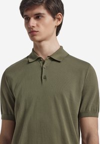 Grön polo skjorta i mjukt tyg, med klassisk krage, treknapps knäppning och korta ärmar med ribbade manschetter.