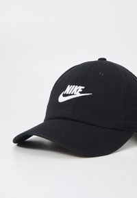 Gorra de béisbol negra hecha de algodón, con un logo de Nike bordado en blanco en la parte frontal y una visera curvada. Diseño y textura simples.