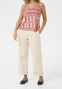 Červený vzorovaný top na tenkých ramínkách, doplněný krémovými širokými kalhotami. Černé baleríny s mašlí dokončují vzhled.