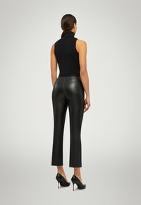 Svart ärmlös polokrage, figurnära design, ihopparad med högmidjade svarta byxor i faux läder, med en slät struktur och kort längd.