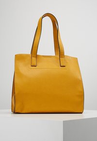 Gul læder tote taske med en tekstureret overflade, to lange håndtag og et struktureret design. Har en glat kant langs kanterne.