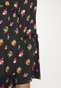 Svart blommig klänning med små färgglada blommönster, med rynkade ärmar och en samlad midja. Mjuk, lättviktsmaterial med en flödande silhuett.