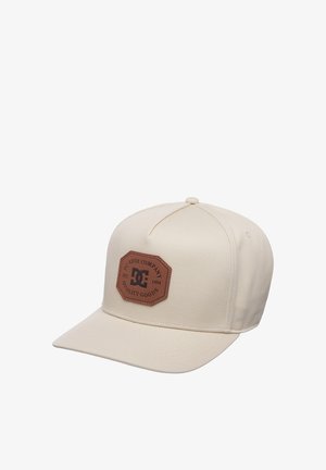 Beżowa czapka z daszkiem z brązową skórzaną naszywką z napisem "DC Shoe Company Quality Goods Est. 1994" na przednim panelu.