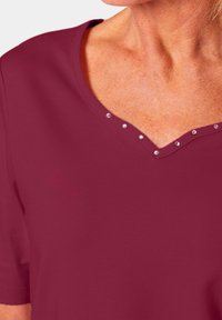 Bordeaux korte mouw top met een V-hals, versierd met kleine, heldere strass steentjes langs de randen. Gladde stoftextuur.