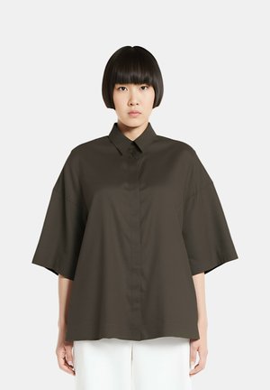 Camicia oversize verde scuro con colletto a punte, maniche corte e chiusura con bottoni. Texture liscia, design minimalista, da abbinare a pantaloni bianchi.