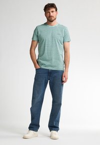 Gestreept T-shirt met korte mouwen in groen met marineblauwe strepen, gecombineerd met een blauwe spijkerbroek. Schoeisel zijn witte sneakers. Eenvoudig casual ontwerp.