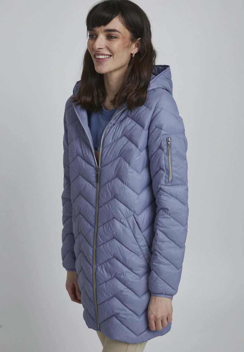 Giacca isolante di un leggero viola con motivo a chevron, dotata di zip sul davanti e cappuccio. Presenta una tasca con zip sulla manica sinistra.
