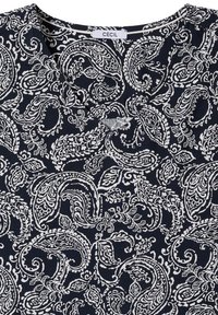 Tissu bleu foncé avec des motifs paisley et floraux blancs complexes et un petit détail en V avec une étiquette de la marque CECIL à l’intérieur du col.