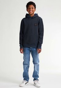 Hanorac bleumarin cu mâneci lungi, buzunar frontal și țesătură texturată; asortat cu blugi albastru deschis și adidași albi.