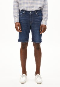 Donkere blauwe denim shorts, met een klassiek vijf-pocket ontwerp, rechte snit en opgerolde zoom. Gecombineerd met witte veterschoenen.