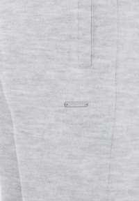 Pantalons de survêtement gris en tissu doux, avec un devant plat, des poches latérales et une étiquette en métal avec "SMILOOY" brodée dessus.