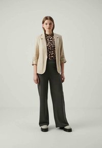 Beiger Leinenblazer über einem Leopardenmuster-Oberteil, kombiniert mit dunklen, gestreiften, weit geschnittenen Hosen und schwarzen Plateauschuhen. Schlichtes, modernes Design.