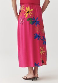 Longue jupe rose ornée de motifs floraux colorés en jaune, bleu, rouge et vert. Fabriquée en tissu doux avec une taille élastique.