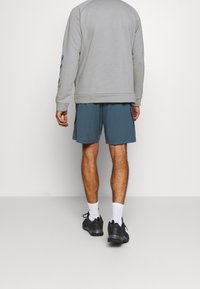 Sweatshirt gris avec ourlet côtelé, associé à un short teal à coupe décontractée. Des baskets noires et des chaussettes blanches complètent la tenue.
