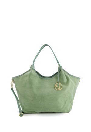 Zachte groene suède handtas met dubbele handvatten, afneembare schouderriem en een ronde gouden hanger die vlak bij de bovenrand hangt.