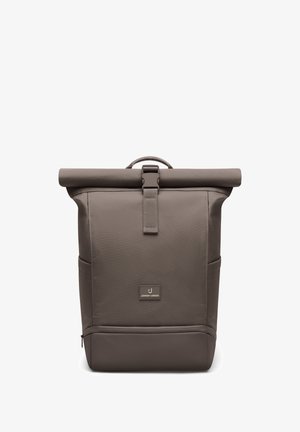 Zaino marrone con chiusura a rotolo con fibbia frontale, tasche laterali, scomparto inferiore con cerniera e una piccola etichetta del marchio sul pannello frontale.