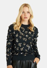 Czarny sweter z teksturowymi, kwiatowymi zdobieniami w metalicznych odcieniach, okrągłym dekoltem i ściągaczami przy rękawach. Miękka tkanina i luźny krój.