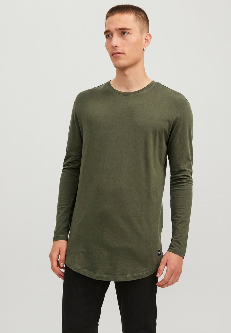 Olijfgroen T-shirt met lange mouwen van zachte katoen, voorzien van een ronde hals en een gebogen zoom, met een zwart label accent aan de zijkant.