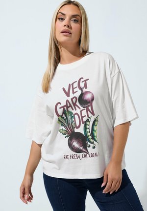 Kobieta o długich blond włosach, ubrana w białą koszulkę z ilustracjami warzyw i tekstem ""Veg Garden Eat Fresh, Eat Local!"" na białym tle.