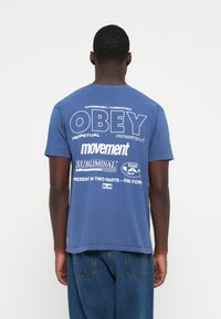 Blue cotton t-shirt featuring white text graphics on the back, with bold lettering and varied typography. Short sleeves, standard fit.