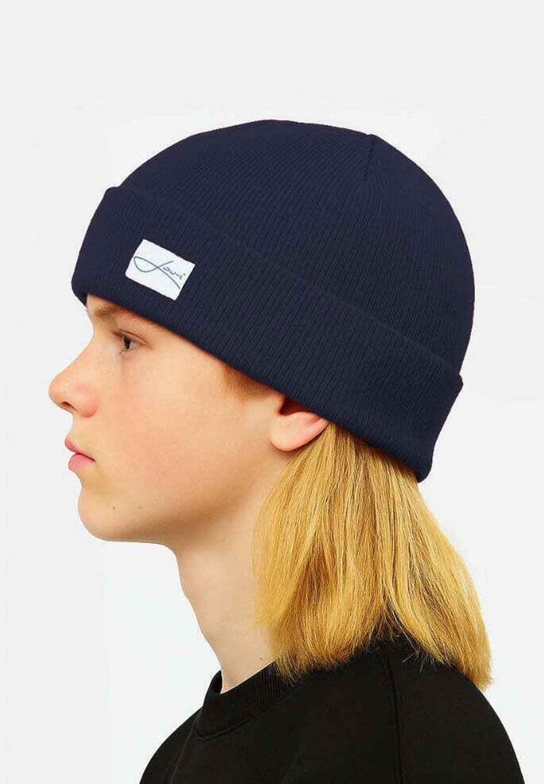 Navy blue ribbed knit beanie with a folded cuff and a white tag featuring a logo, shown on a person with light blonde hair.