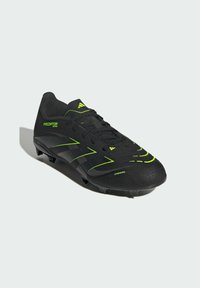 Czarne korki piłkarskie Adidas Predator z neonowymi zielonymi akcentami, teksturowana cholewka, sznurowadła i wymodelowane wkręty na podeszwie do gry na twardym podłożu.