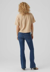 Haut beige texturé à manches courtes, associé à un jean évasé bleu. Le haut a une coupe ample, tandis que le jean possède des poches arrière.