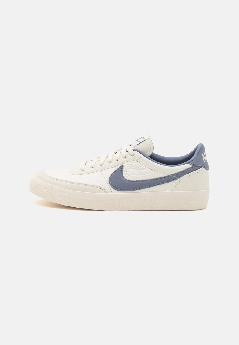 Baskets Nike en cuir crème, avec un design de swoosh bleu, semelle en caoutchouc, bout rond et lacets plats, sur un fond clair.