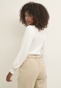 Haut à manches longues côtelé blanc avec une silhouette ajustée et un col rond, assorti à un pantalon beige taille haute avec une ceinture élastique.