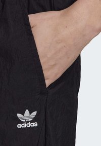 Svart tygficka på träningskläder, med en broderad vit Adidas-logga och en strukturerad yta som framhäver dess lätta design.