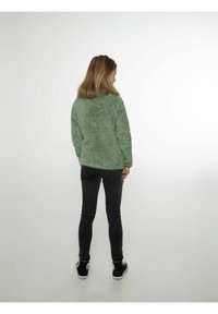 Rozmyty zielony sweter z długimi rękawami, luźny krój i ściągacze, w połączeniu z czarnymi obcisłymi dżinsami i czarnymi sneakerami.