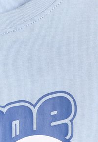 Gros plan sur un tissu bleu clair avec des lettres bulles bleu foncé partielles sur un col rond côtelé.