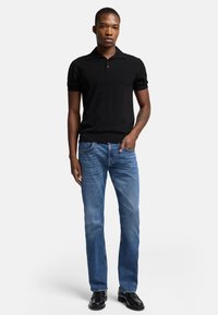 Polo noir à manches courtes associé à un jean droit bleu clair et des chaussures noires. La tenue présente une coupe ajustée et une texture douce.