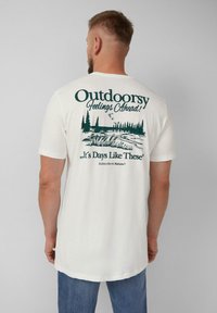 Witte katoenen t-shirt met een groene outdoor-thema grafiek op de achterkant, inclusief bomen en tekst. Korte mouwen en een relaxte pasvorm.