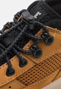 Barna bőr és fekete hálós sneaker, állítható fekete elasztikus fűzőkkel, megerősített fűzőlyukakkal és textúrázott felülettel.