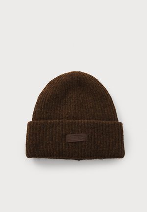 Gorro de punto marrón con textura acanalada, que presenta un borde doblado y un pequeño parche de cuero con texto. Diseño simple y cálido.